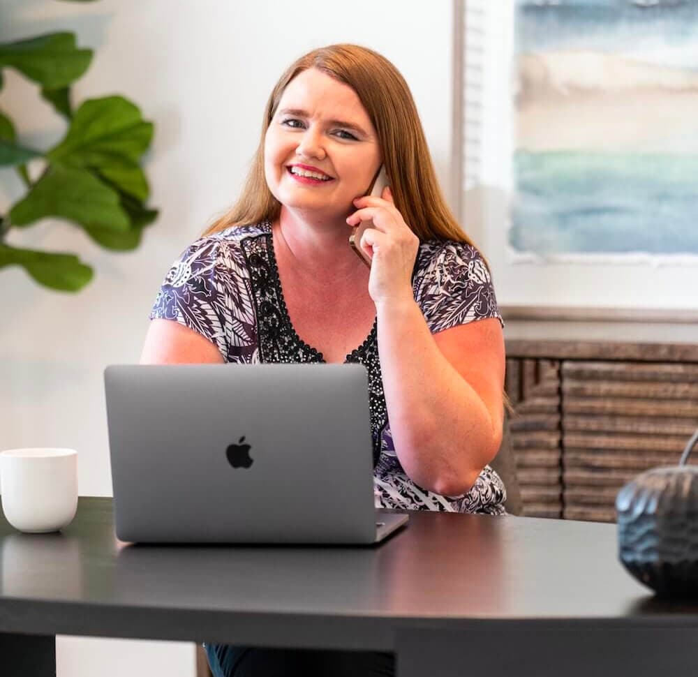 image of woman on phone working on her laptop smiling