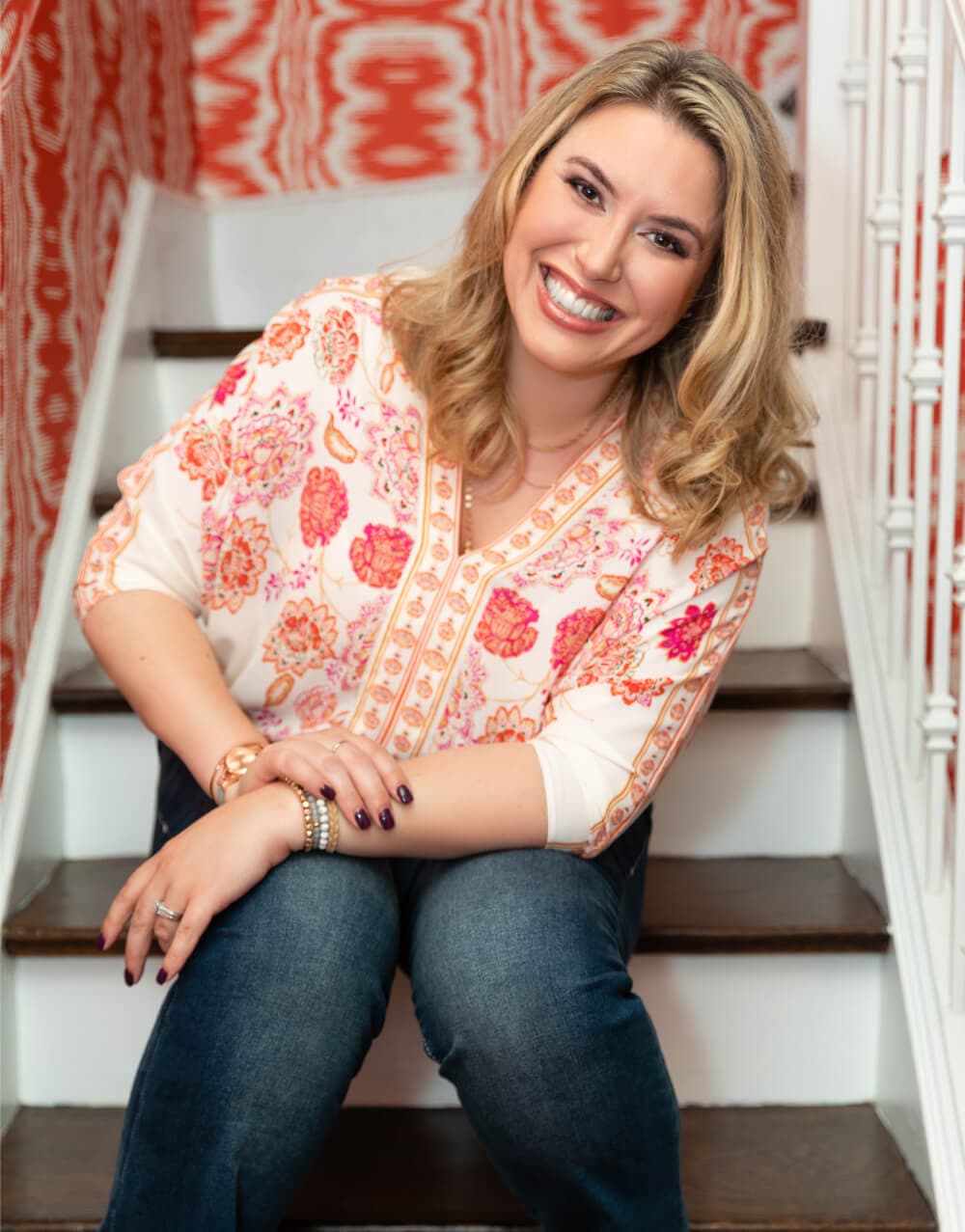 Rebekah sitting on staircase, smiling, wearing jeans and a white and floral pink top